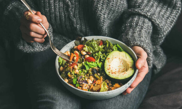 A person holding a bowl of colorful salad with avocado and greens