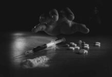 A hand reaching for pills next to a syringe and powder on a table