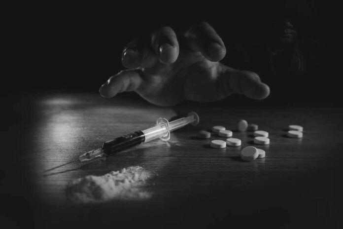shutterstock_2134094607.jpg A hand reaching for pills next to a syringe and powder on a table