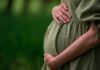The Hidden Benefit of Prenatal Strolls Pregnant woman in a green dress gently holding her belly in a natural setting