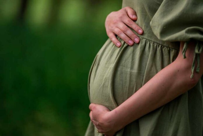 Pregnant woman in a green dress gently holding her belly in a natural setting