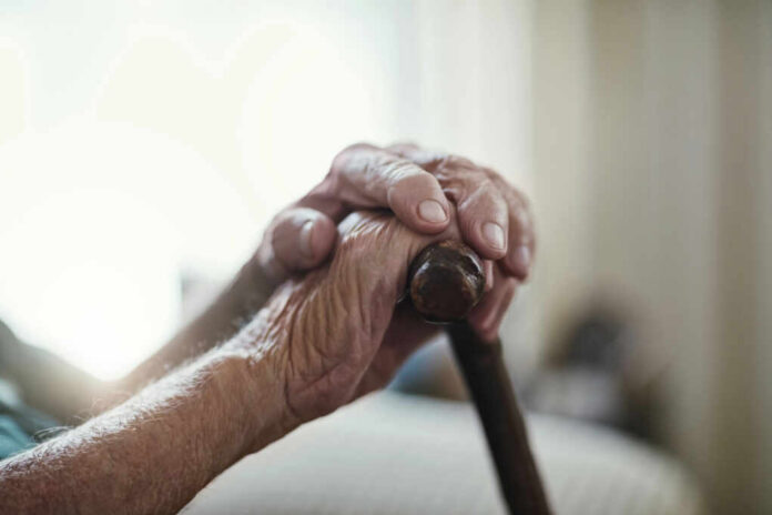 Close-up of elderly hands resting on a cane