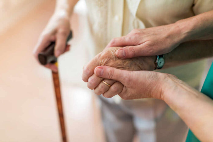 Two hands clasped together, one elderly and one younger, with a cane in the background