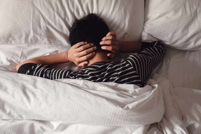 Child lying in bed with hands over ears