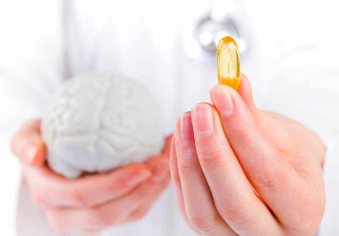 shutterstock_182957405.jpg A medical professional holding a brain model in one hand and a yellow supplement capsule in the other