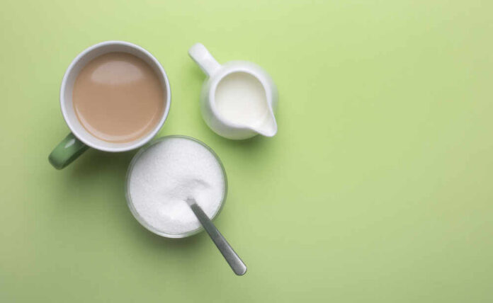 A cup of coffee, a bowl of sugar, and a creamer on a green background