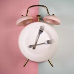 Fasting Frenzy: Why Women Are at Risk An alarm clock with a plate and two forks arranged in a creative design
