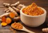 Turmeric powder in a wooden bowl with fresh turmeric roots