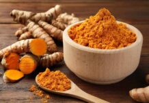 Turmeric powder in a wooden bowl with fresh turmeric roots