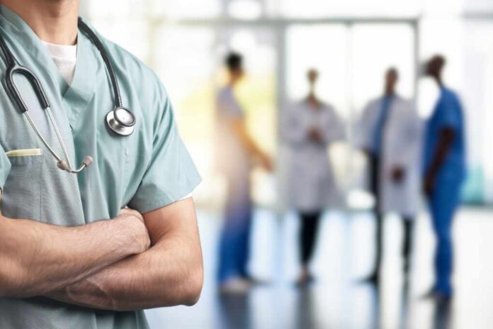 shutterstock_2483848893.jpg A healthcare professional in scrubs with a stethoscope, standing with arms crossed in a hospital setting