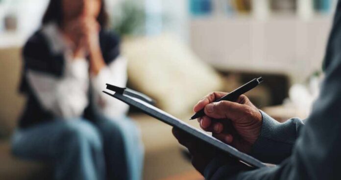 A therapist taking notes during a session with a client in the background