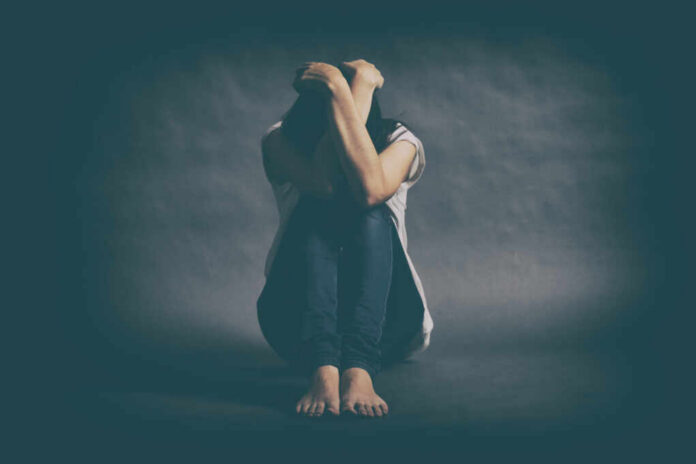 shutterstock_552669553.jpg A person sitting on the floor with their arms wrapped around their knees, conveying a sense of distress