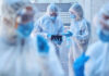 American Doctor’s Ebola Evacuation: Why Germany? Healthcare workers in protective gear discussing information on a tablet outdoors