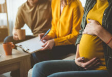 Pregnant woman sitting with two people discussing notes in a cozy living room