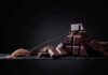 A pile of dark chocolate bars with cocoa powder on a black surface