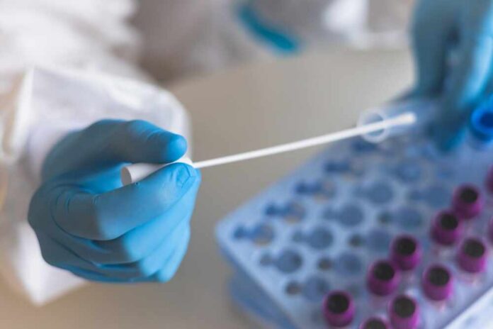 Healthcare professional holding a swab next to a tray of sample vials
