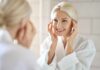 Stagnant Aging: Daily Habits DEFEAT Time Smiling woman in a bathrobe applying skincare in front of a mirror