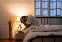 A person sitting on a bed with their head in their hands, expressing distress