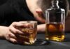 ALARMING Rise in Cancer Linked to Booze A person with their head down, holding a glass of whiskey next to a bottle