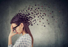 A woman with glasses holding her head, with fragments dispersing from her head