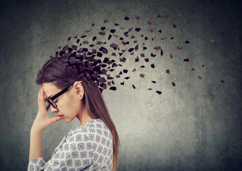 A woman with glasses holding her head, with fragments dispersing from her head