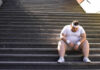 How GLP-1s Sabotages Your Workouts An exhausted man in sportswear sitting on outdoor stairs, looking down.