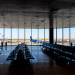 Airport departure lounge with empty seating facing large windows