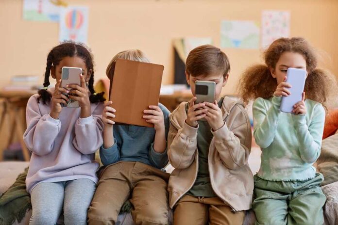 Group,Of,Young,Children,Holding,Smartphones,And,Hiding,Faces,,Gen Four children sitting together, each engaged with their electronic devices