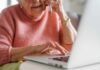 Elderly woman on a phone call while using a laptop