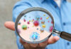 Cancer Cure’s Hidden Saboteur Exposed A person holding a magnifying glass showing colorful microorganisms