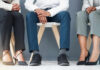 Could Your Shoes Be Ruining Your Feet and Posture? Three individuals in business attire sitting on chairs, showcasing their shoes and legs