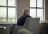 Body Clock Rhythm Linked To Dementia Risk Elderly man sitting in a chair, looking out a window with a thoughtful expression