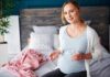 Invisible Toxins That Sabotage Pregnancy Outcomes Pregnant woman sitting on bed holding pills and a glass of water