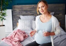 Pregnant woman sitting on bed holding pills and a glass of water