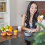 Want Digestive Regularity & Optimal Poops? 2 Ingredients Can Help Woman sitting at kitchen counter holding a supplement bottle