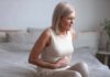 Calcium Intake and Bowel Cancer Risk Woman sitting on bed holding her stomach in pain