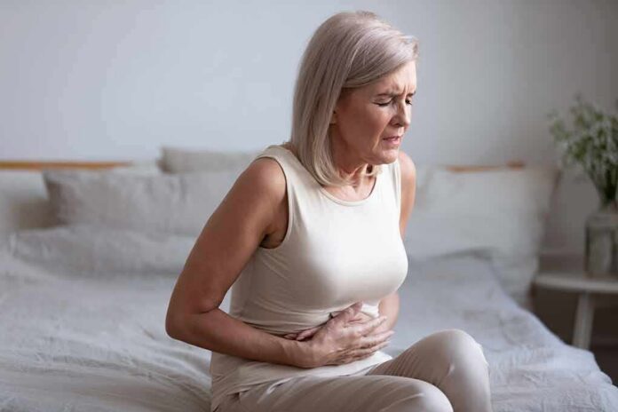 shutterstock_1680034063 Woman sitting on bed holding her stomach in pain