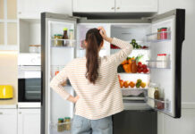 Everyday Breakfast Drink Rewiring Your Genes A woman standing in front of an open refrigerator filled with various fruits and vegetables
