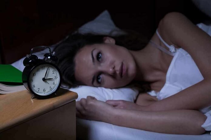 shutterstock_237699745 Woman lying awake in bed beside an alarm clock