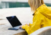 Woman in a yellow raincoat working on a laptop at an outdoor table