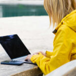 Woman in a yellow raincoat working on a laptop at an outdoor table