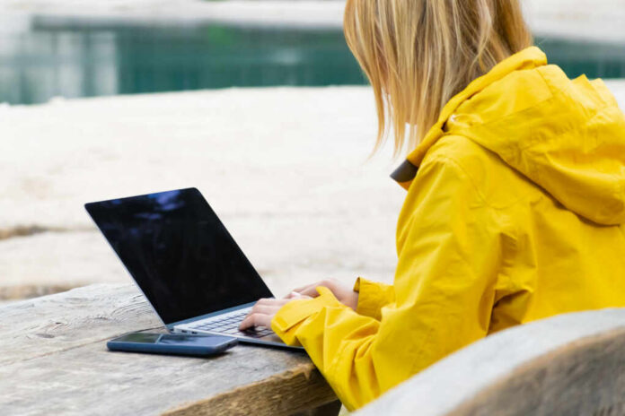 Woman in a yellow raincoat working on a laptop at an outdoor table