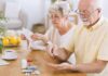 Older man taking pills at a table while woman reads instructions