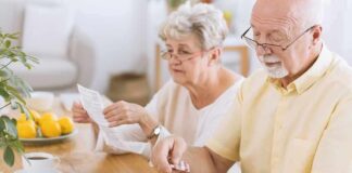 Older man taking pills at a table while woman reads instructions