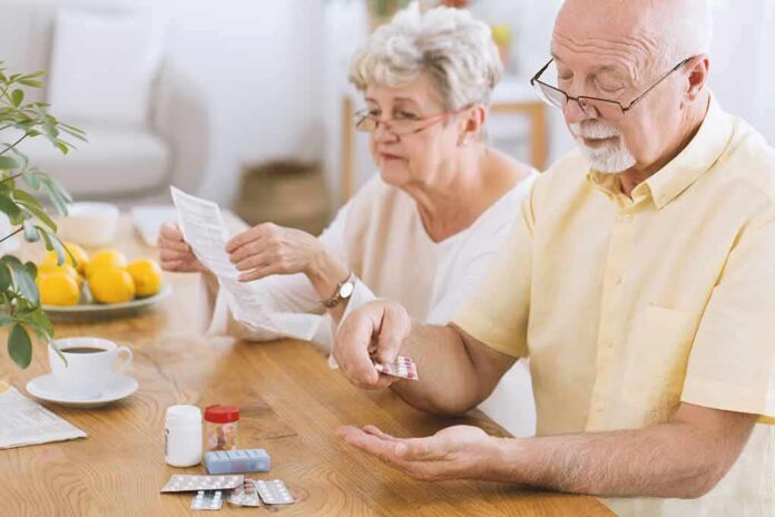 shutterstock_1011163015-2 Older man taking pills at a table while woman reads instructions