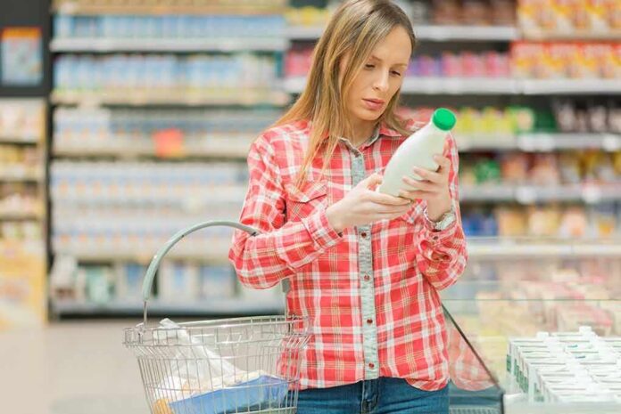 shutterstock_1031614558 Woman reading a bottle label in a grocery store aisle