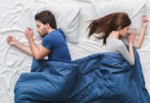 What Is the Scandinavian Sleep Method; and Does It Work? Couple sleeping back to back in bed under blue blanket