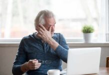 Older adult rubbing eye while holding glasses near a laptop