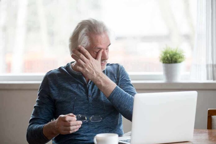 shutterstock_1185179050 Older adult rubbing eye while holding glasses near a laptop