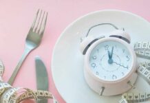Pink alarm clock on a white plate with fork, knife, and measuring tape